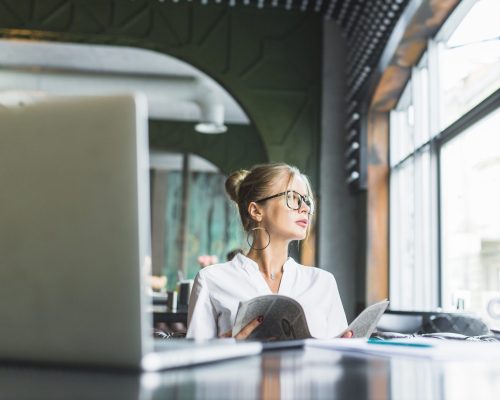 businesswoman-holding-newspaper-with-laptop-desk-caf businesswoman-holding-newspaper-with-laptop-desk-caf